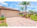 Paver driveway leading to a tan garage with palm trees at 12230 Amica Loop, Venice, FL 34293