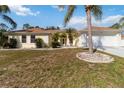 Inviting one-story home with light yellow exterior, lush green lawn, mature palm trees and a two-car garage at 5266 Wagon Wheel Dr, North Port, FL 34291