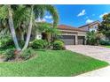 Beautiful home featuring manicured lawn, mature palm trees and lush garden beds on a sunny day at 5511 Foxfire Run, Lakewood Ranch, FL 34211