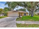 Inviting single-story home with a two car garage, lush green lawn, and mature trees providing shade at 5823 Helen Way, Sarasota, FL 34243