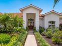 Beautiful front entrance with double doors, white exterior, vibrant landscaping, and a red tile roof, creating a warm welcome at 4492 Del Sol Blvd, Sarasota, FL 34243