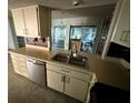 Features a double sink, dishwasher, and cabinetry with a view to the outside enclosed porch with hanging chandelier at 13017 Club Dr, Hudson, FL 34667