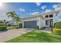 Inviting home featuring a paver driveway, dark garage door, manicured lawn, and tropical landscaping with palm trees at 5187 Barnett Cir, Lakewood Ranch, FL 34211