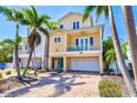 Charming yellow two-story home with balcony, turquoise door, brick driveway, and palm trees at 145 50Th St, Holmes Beach, FL 34217