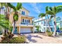 Charming yellow two-story home with balcony, turquoise door, brick driveway, and palm trees at 145 50Th St, Holmes Beach, FL 34217