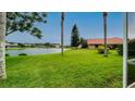 Expansive backyard with a serene pond view, featuring lush grass and palm trees at 5897 Carriage Dr, Sarasota, FL 34243