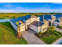 An aerial view of a stunning, modern home with tile roof, lush landscaping, and brick driveway near a serene lake at 17128 Ranchside Pl, Lakewood Ranch, FL 34211