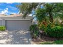 Attached garage with a gray door, brick paver driveway, and lush tropical landscaping at 5417 Champagne # 63, Sarasota, FL 34235