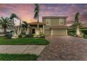 Attractive two-story home boasts a brick driveway, manicured lawn, and tropical landscaping at sunset at 12814 Daisy Pl, Bradenton, FL 34212