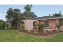 Close-up of the pink brick home featuring arched entryway and tropical landscaping in the front yard at 1308 63Rd Nw St, Bradenton, FL 34209