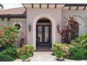 Inviting front entrance with arched doorway, detailed double doors, and colorful, well-maintained landscaping at 7605 Haddington Cv, Lakewood Ranch, FL 34202