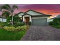 Beautiful single-story home with a lush, landscaped yard and a brick-paved driveway at sunset at 6854 Chester Trl, Lakewood Ranch, FL 34202