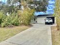 Exterior view of a one-story home with a long driveway and well-manicured lawn and some trees at 3767 Pinstar Ter, North Port, FL 34287