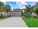 Two-story gray home featuring a gray garage door, tropical landscaping, and a long driveway at 16419 Paynes Mill Dr, Bradenton, FL 34211