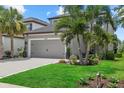 Two-story gray home featuring a gray garage door, tropical landscaping, and a green lawn at 16419 Paynes Mill Dr, Bradenton, FL 34211