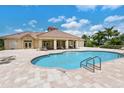 Community pool area surrounded by tan tile flooring and beige tile-roofed structure with seating and lush tropical landscaping at 2937 Seasons Blvd, Sarasota, FL 34240