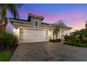 Charming single-Gathering home featuring a two-car garage, paver driveway, lush landscaping, and twilight sky at 2586 Wild Cherry Path, Sarasota, FL 34240