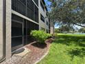 Condo exterior view highlighting a screened-in patio, lush landscaping, and a glimpse of the tennis court at 1999 Kings Hwy # 26A, Punta Gorda, FL 33980