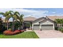 A charming home with a paver driveway, green lawn, and vibrant red flowers nestled around palm trees at 11200 Whimbrel Ln, Sarasota, FL 34238