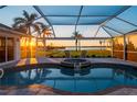 Relaxing pool area with a water feature, screened enclosure, and scenic views of the waterfront at sunset at 5117 Collingswood Blvd, Port Charlotte, FL 33948
