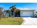 Exterior of a light green home with a metal roof, palm trees, and a white garage door at 18614 Kerrville Cir, Port Charlotte, FL 33948