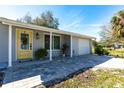 Inviting entrance with a stylish yellow door, brick paved walkway, lush plants and an attached garage at 18379 Meyer Ave, Port Charlotte, FL 33948