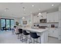 Open-concept kitchen with white cabinetry, stainless steel appliances, pendant lighting and an island with bar seating at 27500 Janzen Ct, Englewood, FL 34223