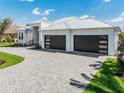 A paved driveway leads to a contemporary home with an attached three-car garage, palm trees, and tidy landscaping at 1631 Casey Key Dr, Punta Gorda, FL 33950