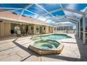 A screened-in pool and spa area featuring a stone patio, with ample seating and a clear blue sky at 16571 Cape Horn Blvd, Punta Gorda, FL 33955
