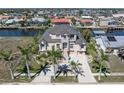 Aerial view of home with water views, lush landscaping, metal roof, and a large concrete driveway in a waterfront community at 250 George Rd, Port Charlotte, FL 33952
