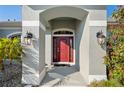 Close-up of a covered front entry with a striking red door, sconce lighting, and decorative stone landscaping at 17 White Marsh Ln, Rotonda West, FL 33947