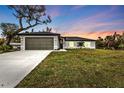 Charming single-story home with a lush green lawn, a two-car garage, and beautiful dusk skies at 267 Camrose St, Port Charlotte, FL 33954