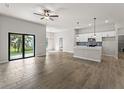 Open-concept living area with wood-look tile flooring, a ceiling fan, kitchen island, and sliding glass doors to the backyard at 17323 Elmwood Ave, Port Charlotte, FL 33948