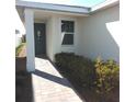 Home exterior view with covered entrance, manicured shrubs, brick paver walkway and gray front door at 43735 Cattleman Dr, Punta Gorda, FL 33982