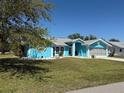 Bright blue single-story home showcasing a lush green lawn, complemented by trees and a gray roof with white trim at 25472 Tevesine Ct, Punta Gorda, FL 33983