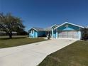 A vibrant blue home features a lengthy driveway, green lawn, and a gray roof with white trim at 25472 Tevesine Ct, Punta Gorda, FL 33983