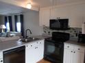 Modern kitchen featuring white cabinets, black appliances, and stylish backsplash, seamlessly connecting to living area at 5421 Holiday Park Blvd, North Port, FL 34287
