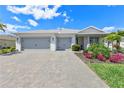 Single-story home featuring a spacious three-car garage and beautiful landscaping with colorful flower beds and a brick driveway at 16064 Shoreline Dr, Punta Gorda, FL 33982
