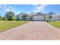 Inviting single-story home with a long brick driveway leading to an attached garage and well-maintained landscaping at 1871 Braddock Ave, North Port, FL 34288