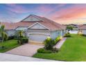 Beautiful single-story home with a well-manicured lawn, tiled roof, and a paved driveway under a colorful sky at 1940 Scarlett Ave, North Port, FL 34289