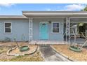 Home exterior showcasing a covered porch with decorative columns, a blue door, and gravel landscaping at 103 Curtis Ne Ter, Port Charlotte, FL 33952
