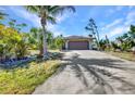 Charming single-story home featuring a two-car garage, long driveway, and lush landscaping with palm trees at 1357 Le Pera Rd, Englewood, FL 34223