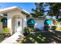 Close-up of the home's front door and well-manicured landscaping with green awnings on the windows at 1381 Fargo St, Port Charlotte, FL 33952