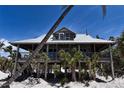 Elevated beach house showcasing a metal roof and a wraparound porch in a tropical setting at 8754 King St, Placida, FL 33946