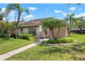 This exterior view features a well-maintained lawn, complemented by lush tropical landscaping, including mature palm trees at 5390 Brassy Loop, North Port, FL 34287
