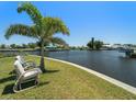 Relaxing waterfront backyard featuring lush grass, a swaying palm tree, and comfortable seating for enjoying the peaceful view at 21444 Higgs Dr, Port Charlotte, FL 33952