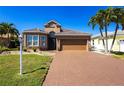 Beautiful house with a brick driveway, lush green lawn, and lovely palm trees against a clear blue sky at 10227 Windsong Rd, Punta Gorda, FL 33955