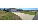 Wide concrete driveway leading to a light gray home with green grass lawn and light-colored brickwork at 18519 Alphonse Cir, Port Charlotte, FL 33948