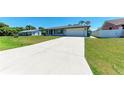 Single-story home with an expansive driveway leading to a one-car garage, surrounded by a lush green lawn at 309 Aurora St, Port Charlotte, FL 33948