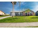 Inviting home featuring a lush green lawn, mature palm trees, and a neutral-toned exterior at 13449 Muriel Ave, Port Charlotte, FL 33981